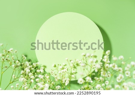 Spring minimal green scene for beauty cosmetic product presentation made with circle geometric shape and wild flowers on a green background. Top view.