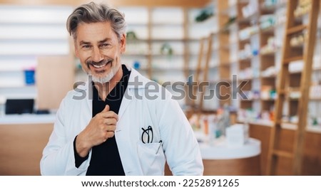 Doctor standing in a pharmacy in a lab coat. Mature healthcare worker smiling at the camera. Senior man working in a chemist. Royalty-Free Stock Photo #2252891265