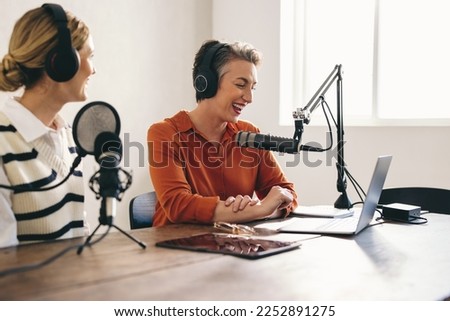 Happy female podcasters having a god time while co-hosting an audio broadcast in a home studio. Smiling content creators recording an internet podcast for their social media channel.