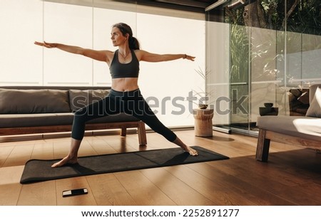 Active senior woman doing the warrior pose during a session of yoga. Mature woman doing a balance exercise on a yoga mat. Sporty woman practicing a healthy workout routine at home. Royalty-Free Stock Photo #2252891277