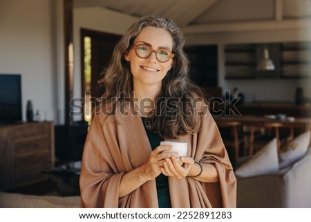 Portrait of a happy senior woman smiling at the camera while standing with a cup of tea in her hands. Cheerful senior woman enjoying a serene retirement at home. Royalty-Free Stock Photo #2252891283