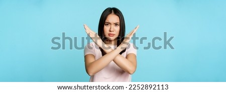Stop. Concerned asian woman showing cross sign, saying no, raise awareness, standing over blue background.