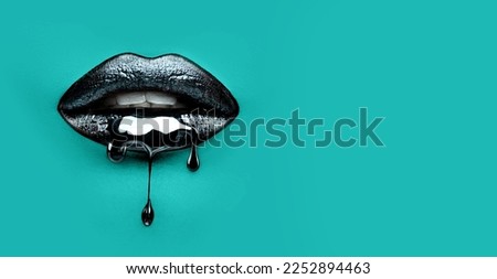 Black Paint dripping from the lips, dark liquid drops on beautiful model girl's mouth on blue background. Halloween party make-up, gothic style. Beauty makeup close up. Wide screen art backdrop. Art