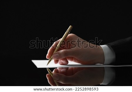 Woman writing on sheet of paper at glass table, closeup