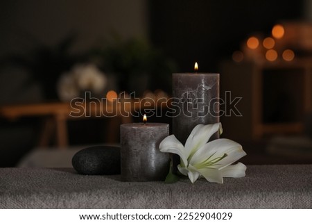 Spa composition with burning candles, lily flower and stone on massage table in wellness center