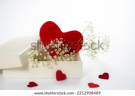 Red heart from felt in a white gift box with gypsophila or baby breath flowers, love symbol for mothers day or valentines day, light background, copy space, selected soft focus, narrow depth of field