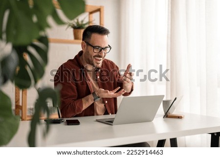 Smiling businessman working on laptop at home office. Young  freelancer or remote teacher using laptop, remote studying, virtual training,  participating in online education webinar at home office. Royalty-Free Stock Photo #2252914463