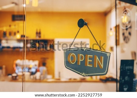 Open sign on glass door in coffee shop, retail store. Local small businesses at food and drink service.
