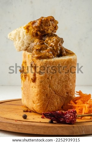 Meat and vegetable curry in white bread vertical photo, close-up. Bunny chow