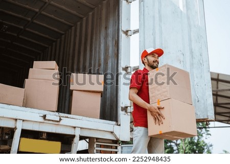 asian delivery man in red uniform lifting package box from container Royalty-Free Stock Photo #2252948435