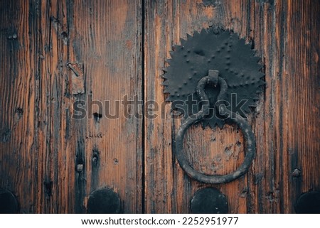 Worn medieval wooden door in brown vintage textured with rusted cast iron door knob.