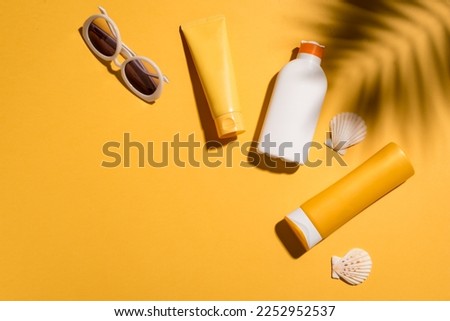 Sunblock lotion bottles and sunglasses on yellow background, copy space. Summer vacation and skin care concept, sunscreen, spf uv-protect cosmetics.