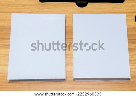 A couple of the white colored hardcover books laying out on the top of a table with wooden texture and some decorations arranged around it, hardcover mockup template image
