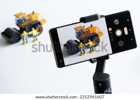 Smartphone on a gimbal selfie stick for photo-video, filming toy construction machinery and workers. Concept of live broadcast construction, video blogging, podcasts, streaming and journalism. 