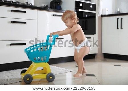 Cute baby with toy walker in kitchen. Learning to walk