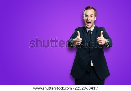 Happy excited businessman showing two thumbs up like hand gesture, in black confident suit, on violet purple background. Very cheerful man. Copy space for ad, slogan or text.