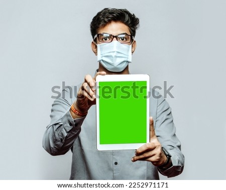 Green mockup screen for ad copyspace free space. Medical professional in mask holding green screen tablet in vertical position with copy space isolated in green background.