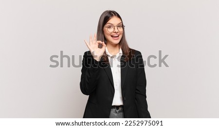 young business woman feeling successful and satisfied, smiling with mouth wide open, making okay sign with hand