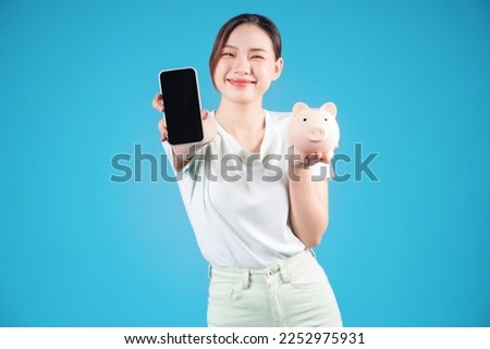 Photo of young Asian woman holding piggy bank on background