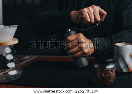 Professional barista making filtered drip coffee in coffee shop. Close up of hands barista grinding coffee beans with hand grinder, pour over coffee with hot water and filter paper in cafe. Royalty-Free Stock Photo #2252983109