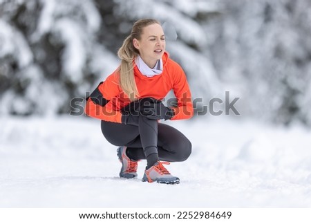 A young fit woman holds a reinforced knee after straining her cruciate ligament during cross-country training in the snow during the winter season. Royalty-Free Stock Photo #2252984649