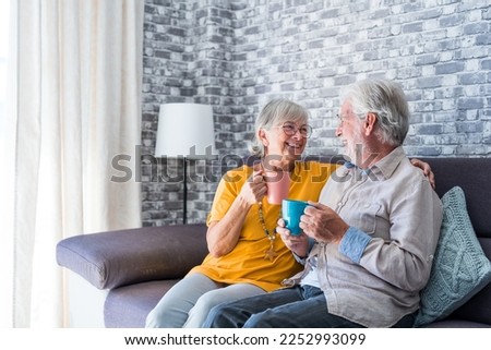 Happy mature 50s husband and wife sit rest on comfortable sofa in living room enjoy tea talking, smiling elderly 60s couple relax on couch at home drink coffee chat speak laugh on leisure weekend Royalty-Free Stock Photo #2252993099
