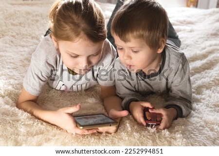 Children are lying on the bed, watching cartoons, playing a game on a smartphon.