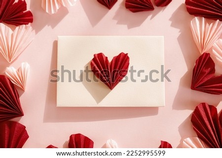 Happy Valentine's day! Stylish envelope with pink and red hearts flat lay on pink paper background. Modern valentine heart cutouts. Love letter. Creative composition