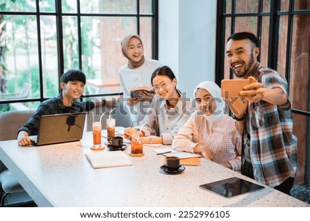 a group of young asian people smiling while taking selfie using cell phone in cafe