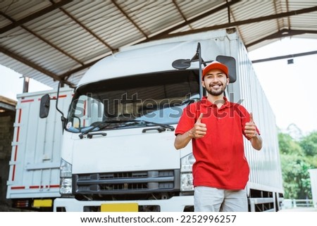 delivery man driver in red uniform smiling with thumbs up in front of delivery truck Royalty-Free Stock Photo #2252996257