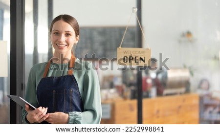 Portrait of happy waitress standing at restaurant entrance and holding digital tablet. 