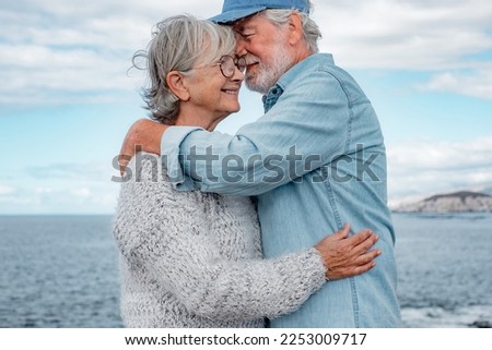 Happy beautiful senior couple tenderly embracing by the sea. Smiling elderly man and woman enjoying retirement outdoor trip together