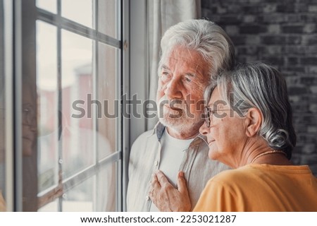 Pensive elderly mature senior man in eyeglasses looking in distance out of window, thinking of personal problems. Old woman wife consoling and hugging sad husband, copy space