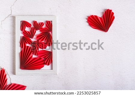 Red paper DIY hearts in an empty photo frame and leaves on a concrete background.