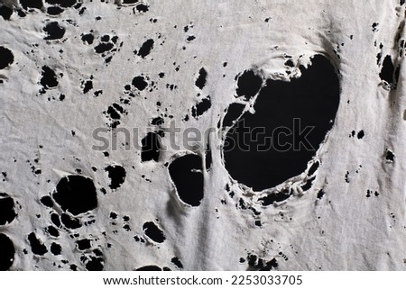 old dirty ragged shirt with holes, grunge damaged cloth on black background, ripped white fabric with many holes Royalty-Free Stock Photo #2253033705