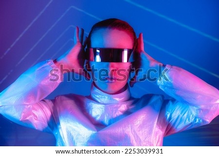Neon portrait of woman, dressed in futuristic holographic clothes and glasses. Portrait of a cyberpunk girl. Neon blue and pink light. Virtual reality glasses. Fashion, futuristic generation concept.