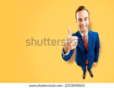 Full body businessman in blue suit showing thumb up like, agree hand sign gesture on yellow background. Comic look happy man. Cartoon style character with big head. Funny face. Copy space mockup area.