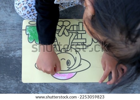 A little girl coloring a picture with colored sand. Cartoon character.