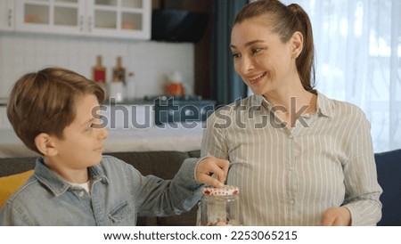 Young mother and her little son putting coins in piggy bank while sitting on sofa at home. The mother teaches the child to be thrifty, to save money, to think about the future, to save.