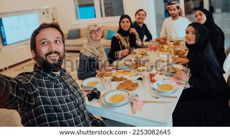 Eid Mubarak Muslim family having Iftar dinner taking pictures with smartphone while eating traditional food during Ramadan feasting month at home. The Islamic Halal Eating and Drinking Islamic family
