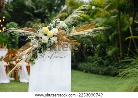 White welcome board sign with a beautiful flower and rustic decoration, standing in front of wedding entrance.