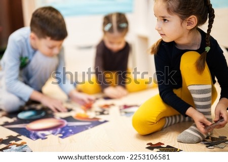 Children connecting jigsaw puzzle pieces in a kids room on floor at home.  Fun family activity leisure. 