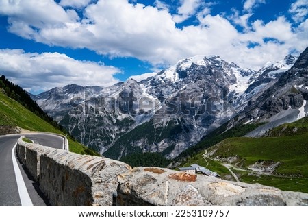 Curvy road that leads through the mountains. Amazing bright colorful spring and summer landscape. Green grass, blue sky with clouds and snowy peaks. Natural landscape, Europe.