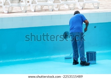 Unrecognizable worker repainting swimming pool in blue colour. Reconstruction process Royalty-Free Stock Photo #2253115489