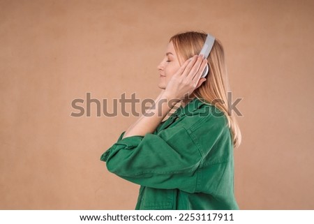 Pretty young woman girl in a stylish green jacket posing isolated on pastel wall background studio portrait. People emotions lifestyle concept. Mock up copy space. Listen music with headphones. 