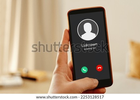 Female hand holding a mobile smartphone displaying an incoming call from unknown caller. Phone suspected spam call concept. Royalty-Free Stock Photo #2253128517