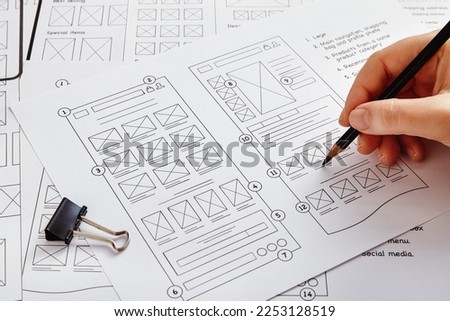 Web design project concept. Close up photo of a UX designer working on website project with a large number of wireframe sketches. Royalty-Free Stock Photo #2253128519