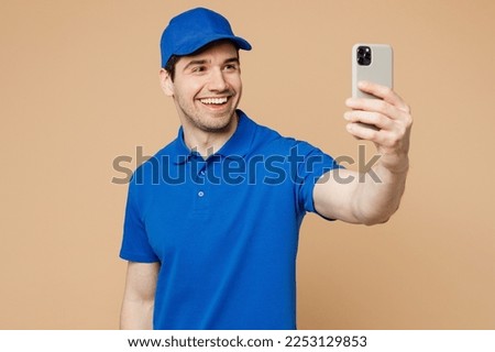 Professional fun delivery guy employee man wear blue cap t-shirt uniform workwear work as dealer courier do selfie shot on mobile cell phone isolated on plain light beige background. Service concept