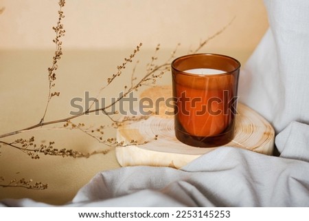 Meditation space with scanted candle. Burning candle on wooden coaster. Warm interior aesthetic composition with dry boho branch and grey fabric. Home comfort, spa, relax and wellness concept, banner Royalty-Free Stock Photo #2253145253