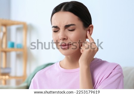 Young woman suffering from ear pain at home Royalty-Free Stock Photo #2253179619